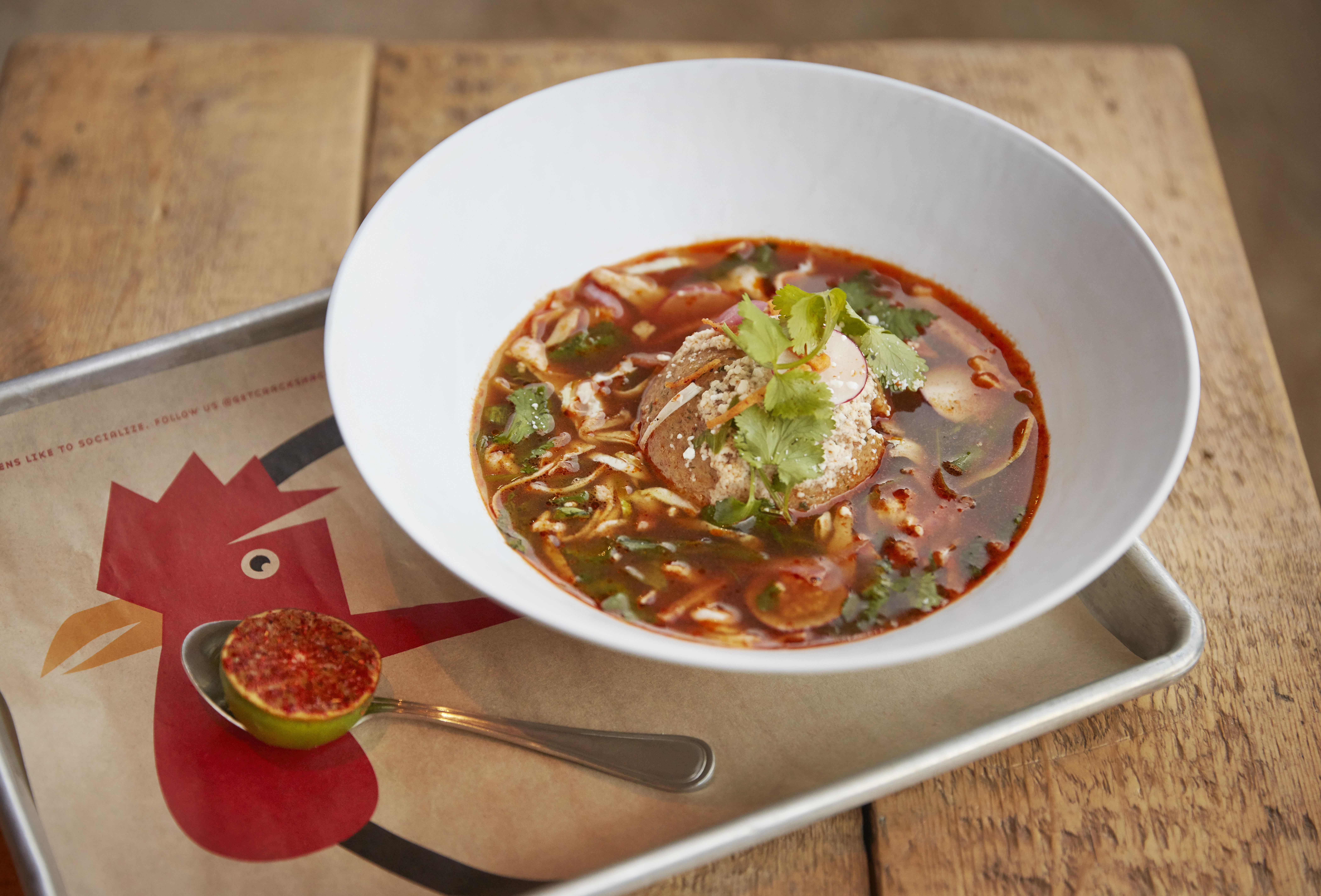 Matzo ball posole in a bowl on a tray next to a lime.