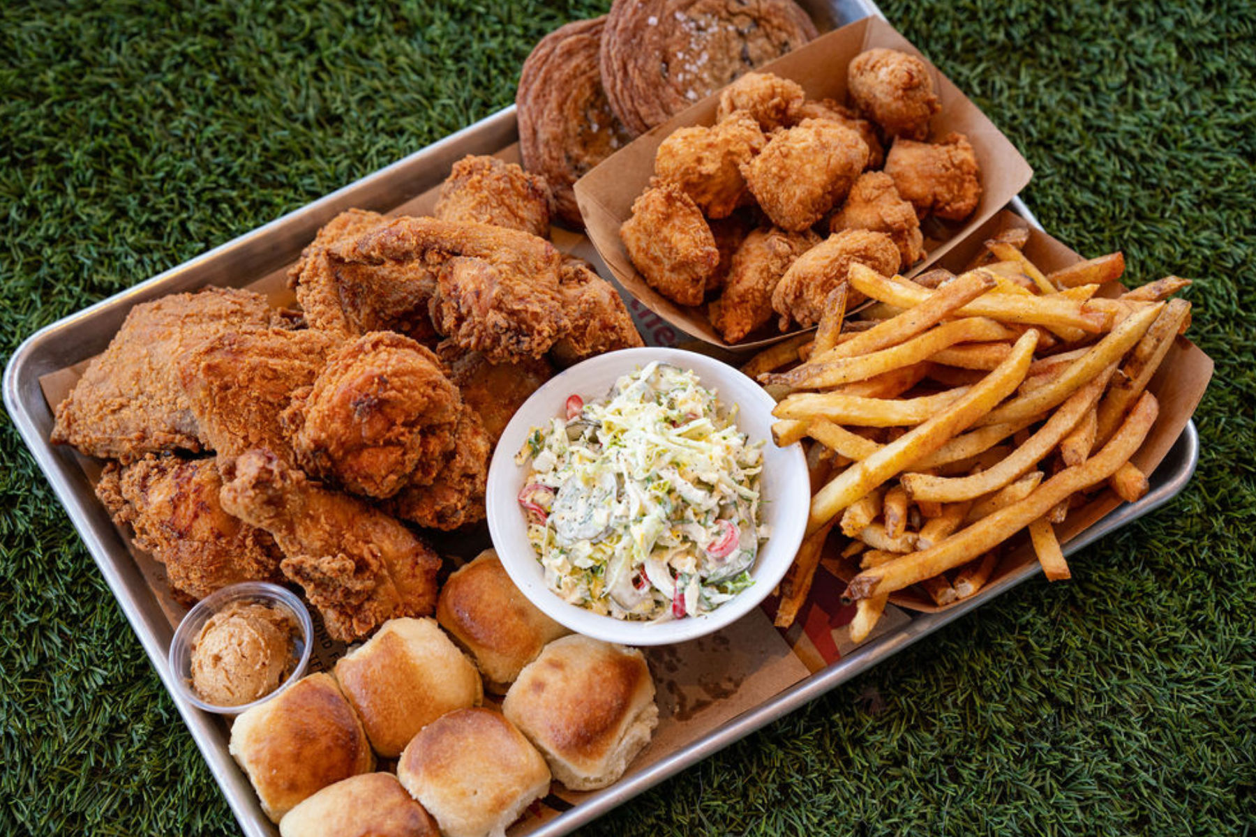 Tray of fried chicken, biscuits, fries, nuggets, and cole slaw on grass