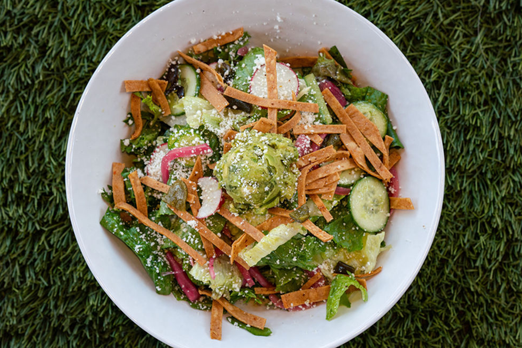 Bowl with salad, guacamole, and tortilla crisps on grass