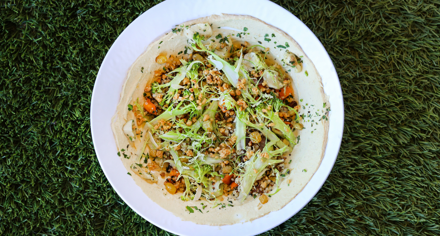 Bowl of vegetables and hummus on fake grass.