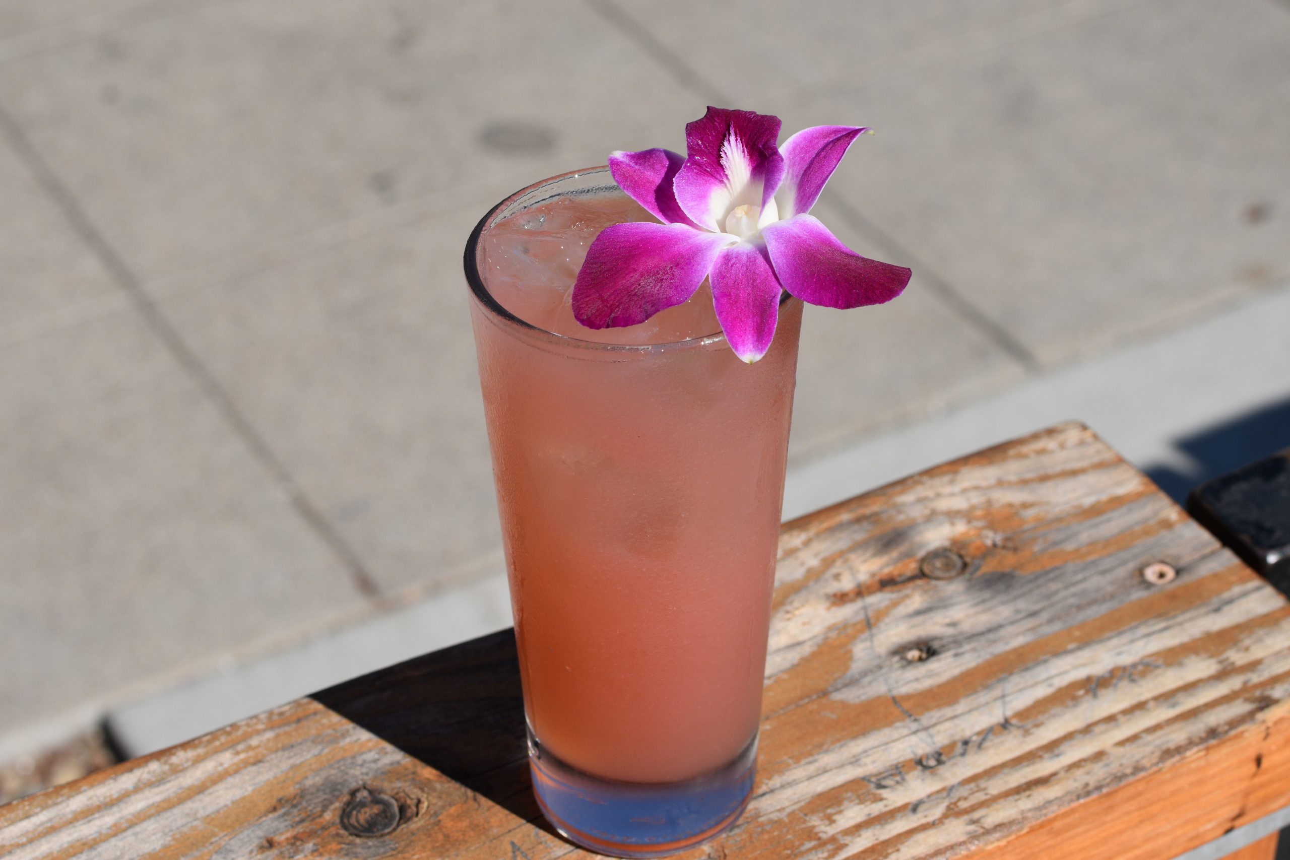 Pink cocktail with a flower garnish on a ledge.