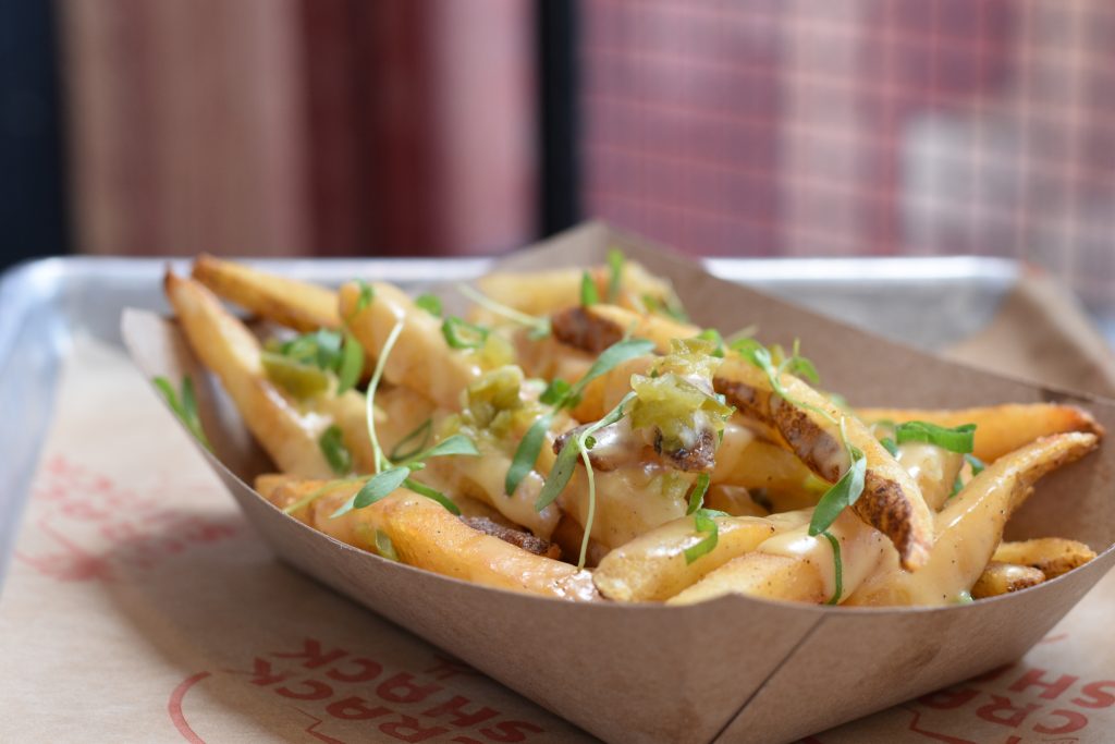 Cheesy fries topped with green herbs in a boat on a tray,