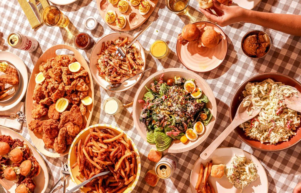 Plates and trays of food on a table with a checkered tablecloth.