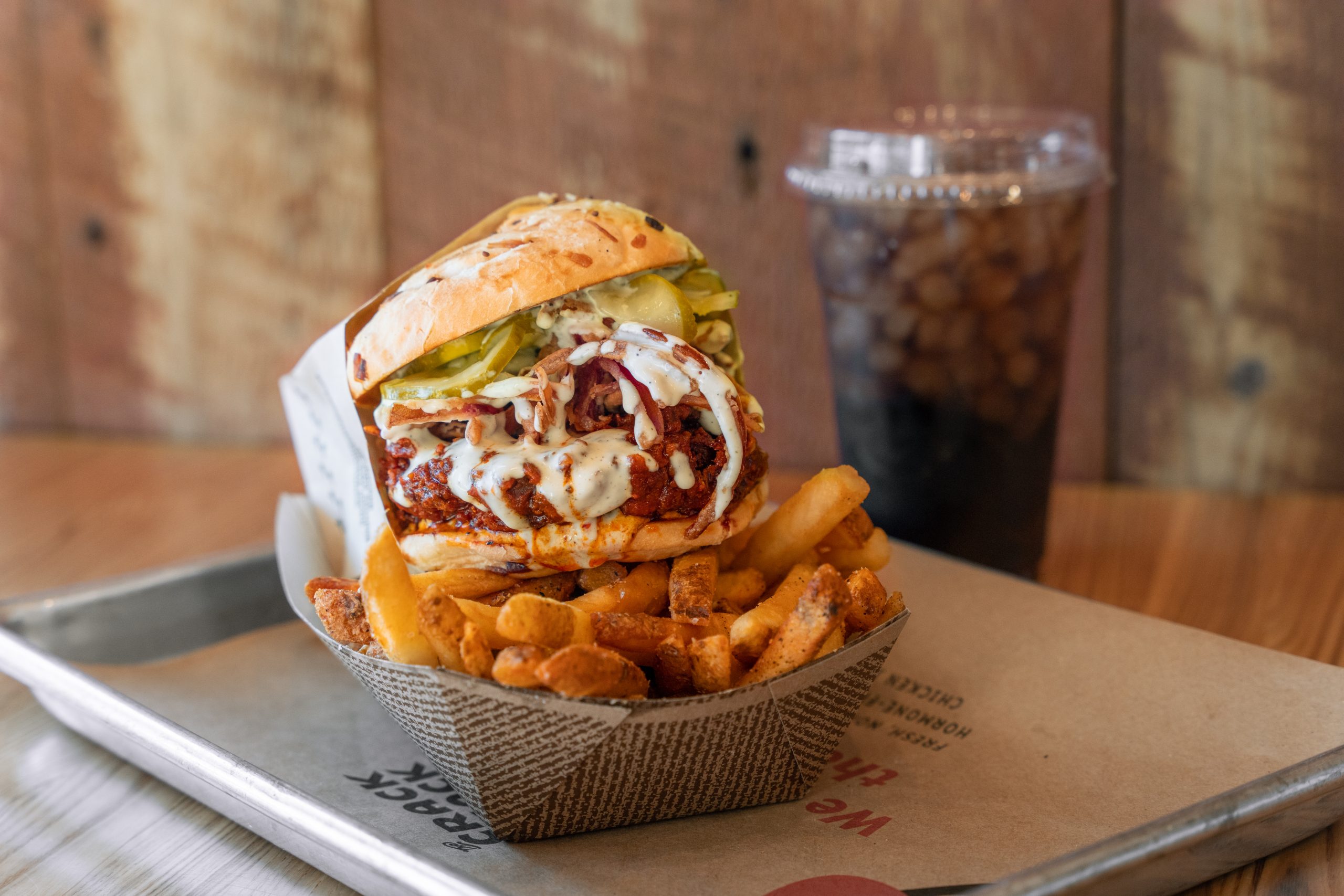fried chicken sandwich on fries in a boat with a fountain drink in the background.