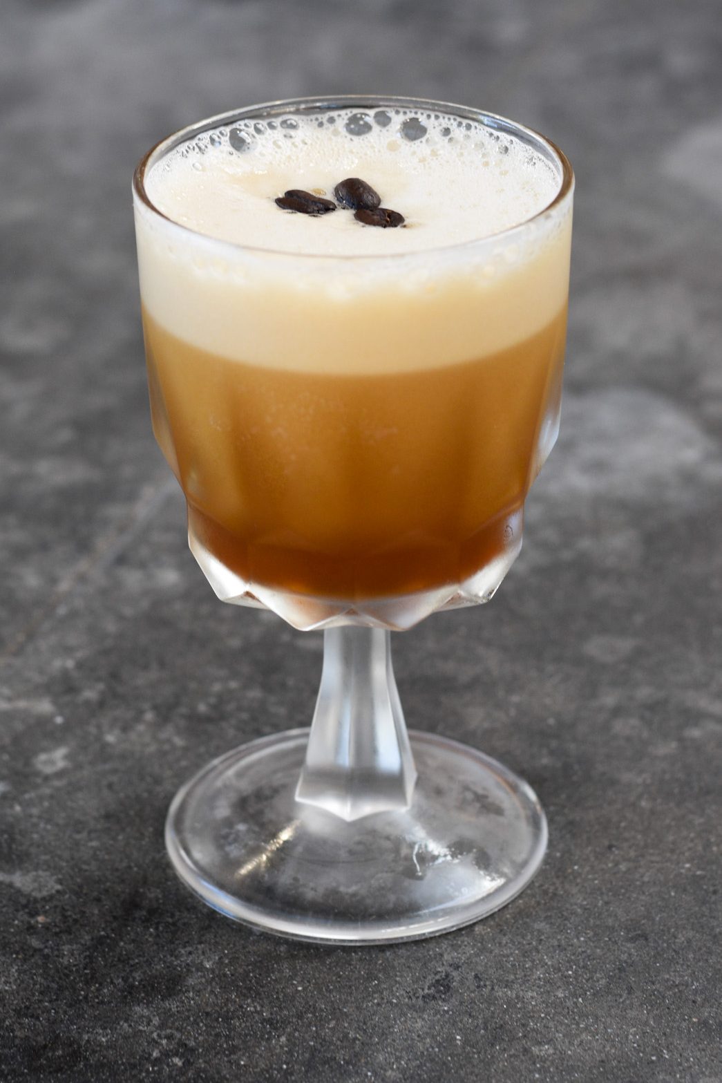 Coffee cocktail in a glass with coffee beans on top on a ledge,