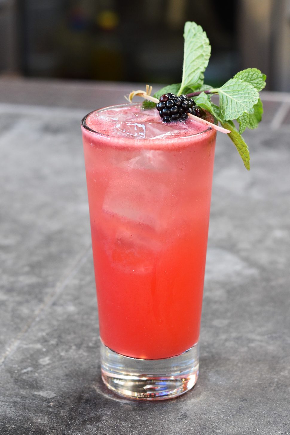 Pink cocktail with a blackberry and mint garnish on a concrete ledge.