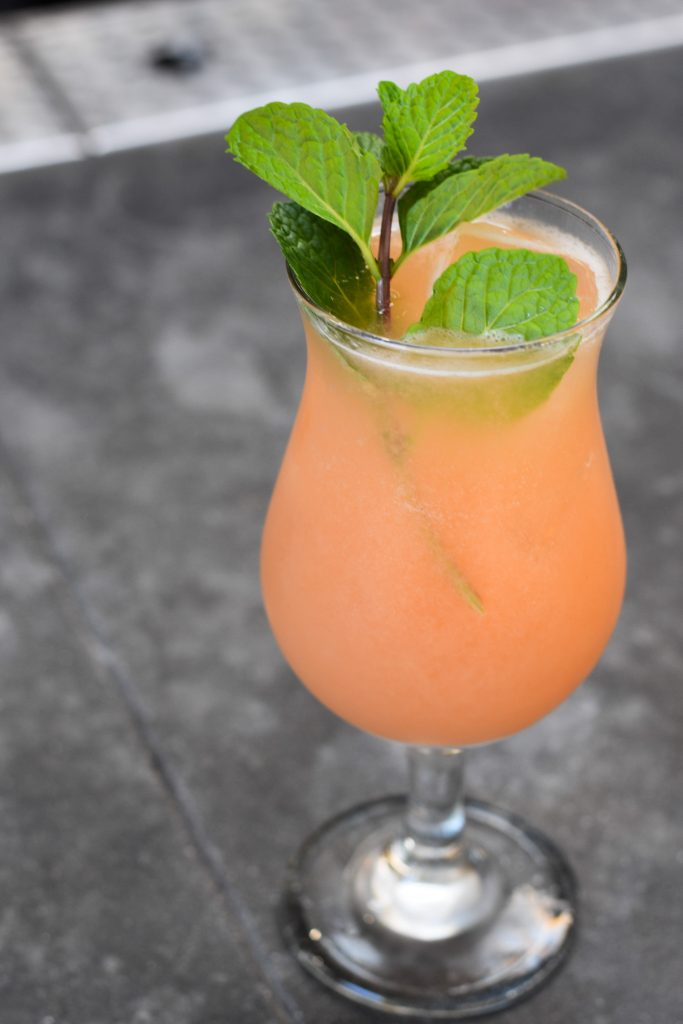 Orange cocktail with a mint garnish on a concrete ledge.