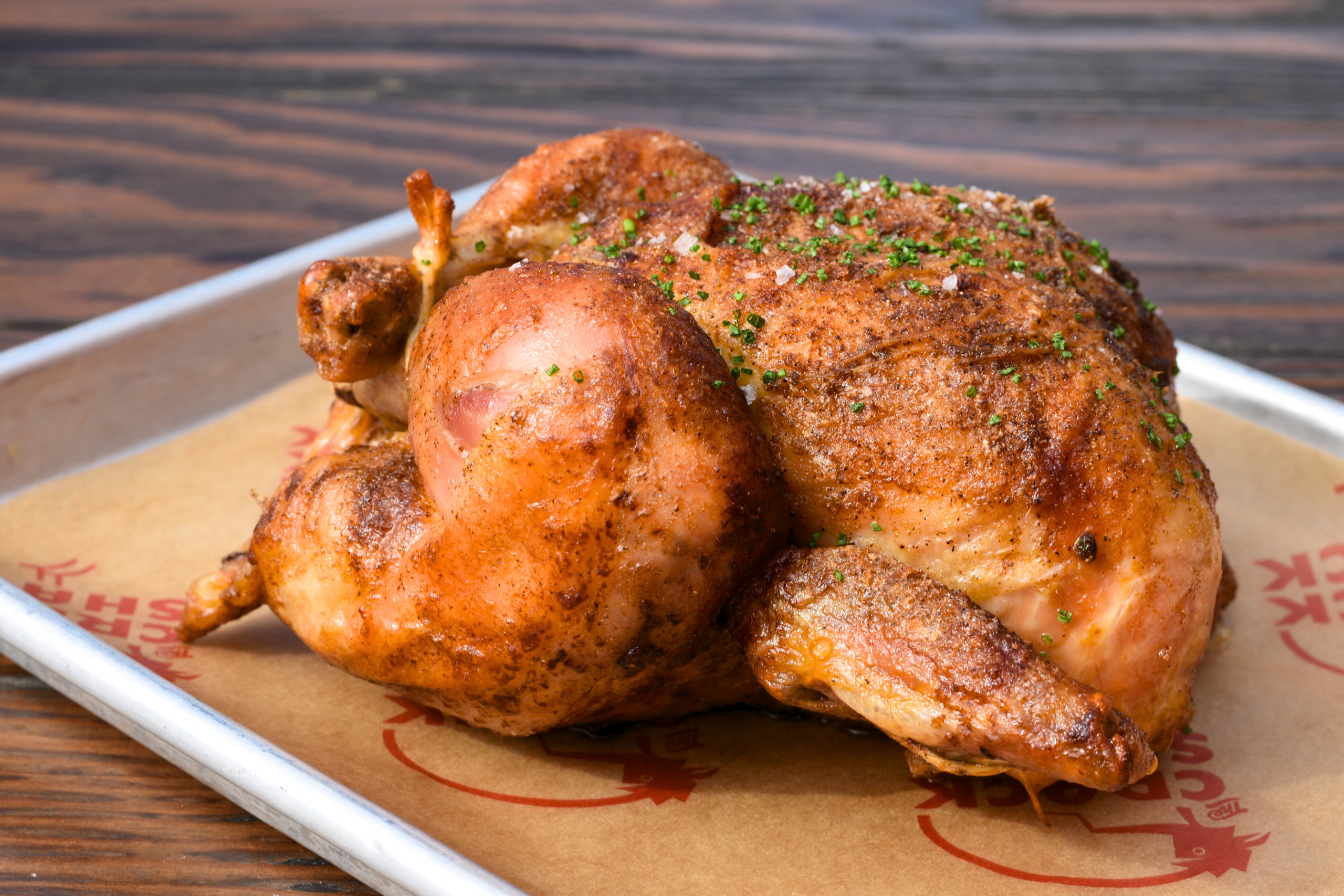 Whole rotisserie chicken with herbs on a tray.