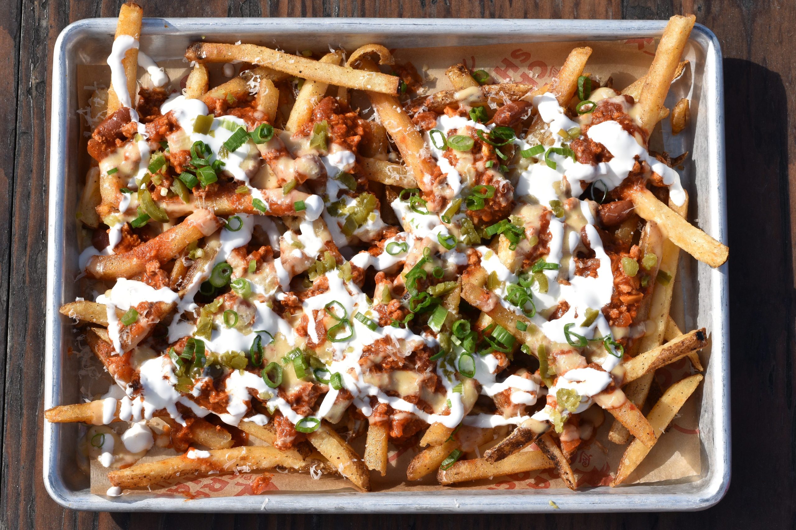 Fries topped with chicken chili, sauces, and garnishes on a tray.