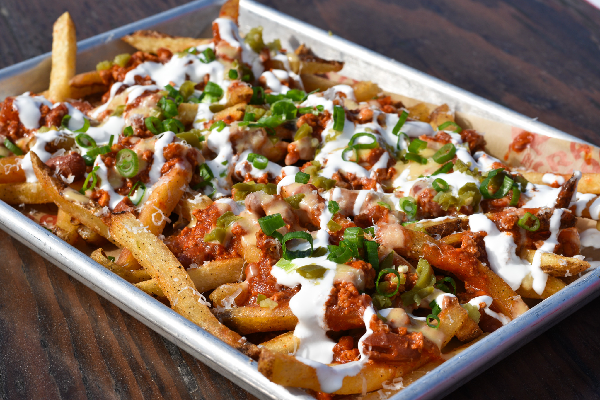 Loaded chili cheese fries on a tray with garnishes.