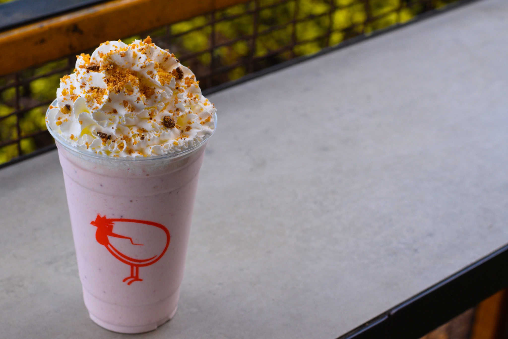 Strawberry shake with whipped cream and crumble on a ledge.