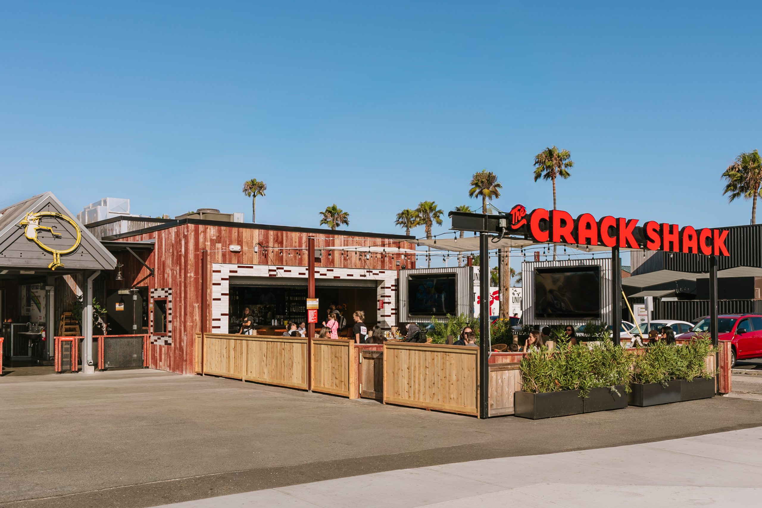 The Crack Shack sign in front of a patio with people on it enjoying food and drinks.
